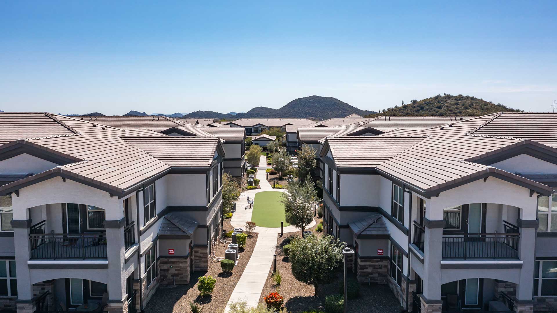 Aerial view of a modern residential complex with symmetrical buildings and a central garden in a hilly landscape.