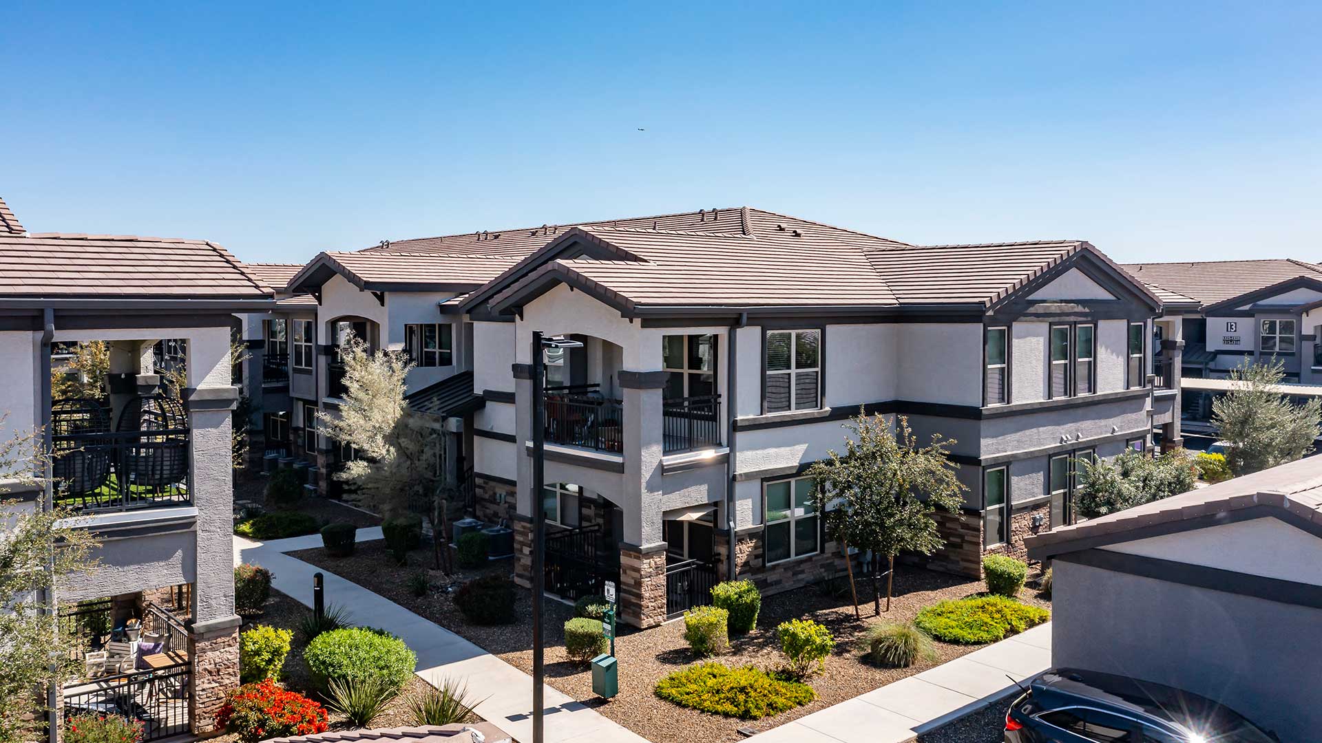 Aerial view of a modern suburban apartment complex with neatly landscaped areas and multiple parked cars.