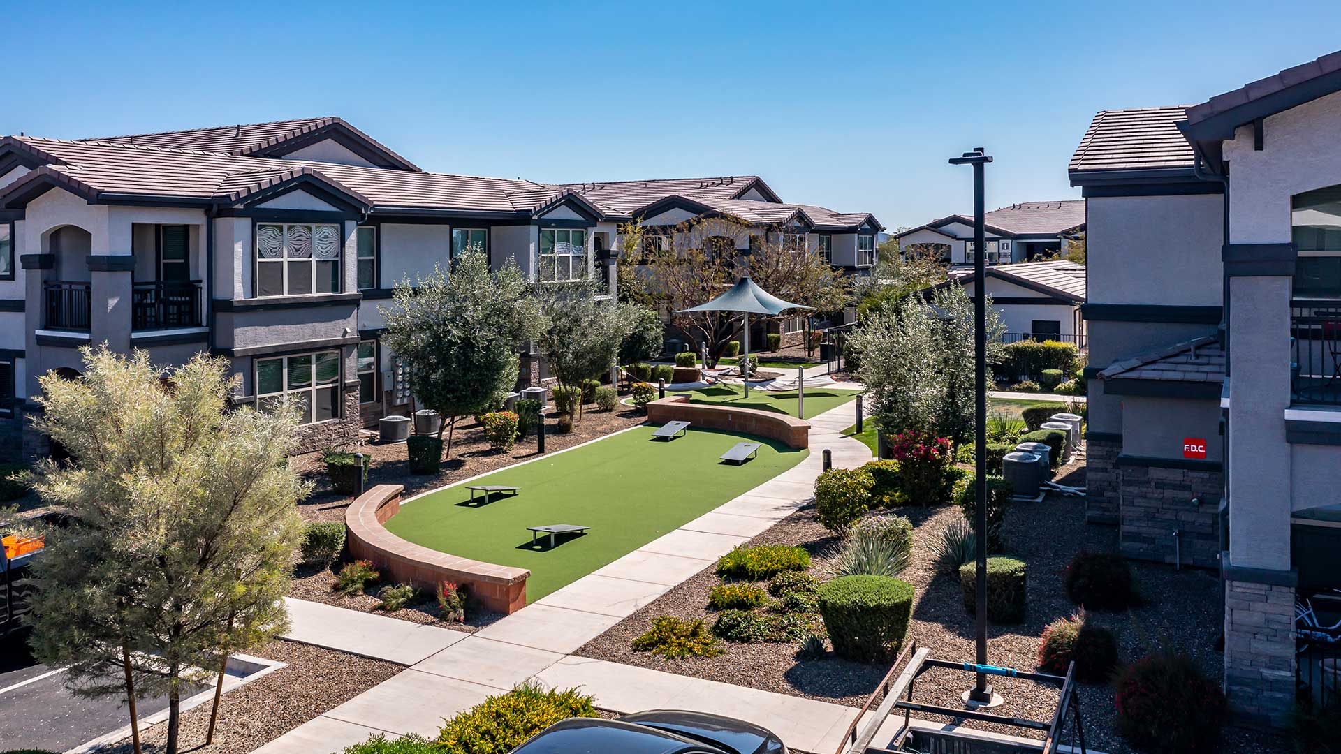 Aerial view of a contemporary apartment complex with green lawns, walking paths, and shaded seating areas under a clear blue sky.