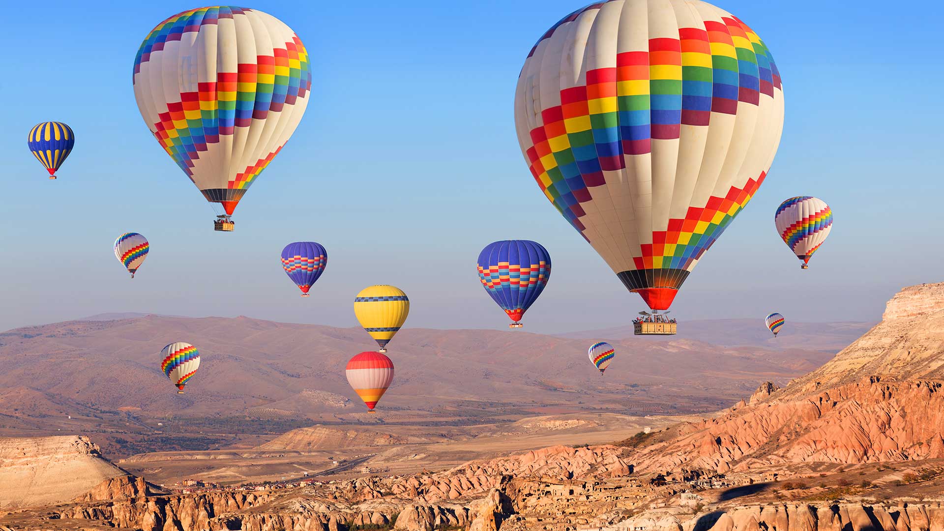 Colorful hot air balloons floating above a rugged landscape at sunrise.